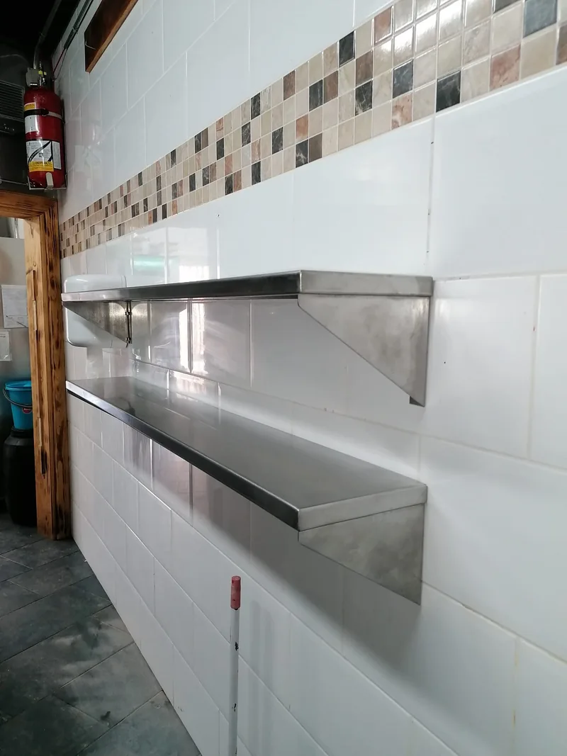 Dos baldas metálicas con soportes triangulares fijadas a una pared alicatada