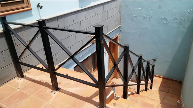 Barandilla negra de postes cuadrados y diagonales en cruz junto a una escalera exterior de baldosas