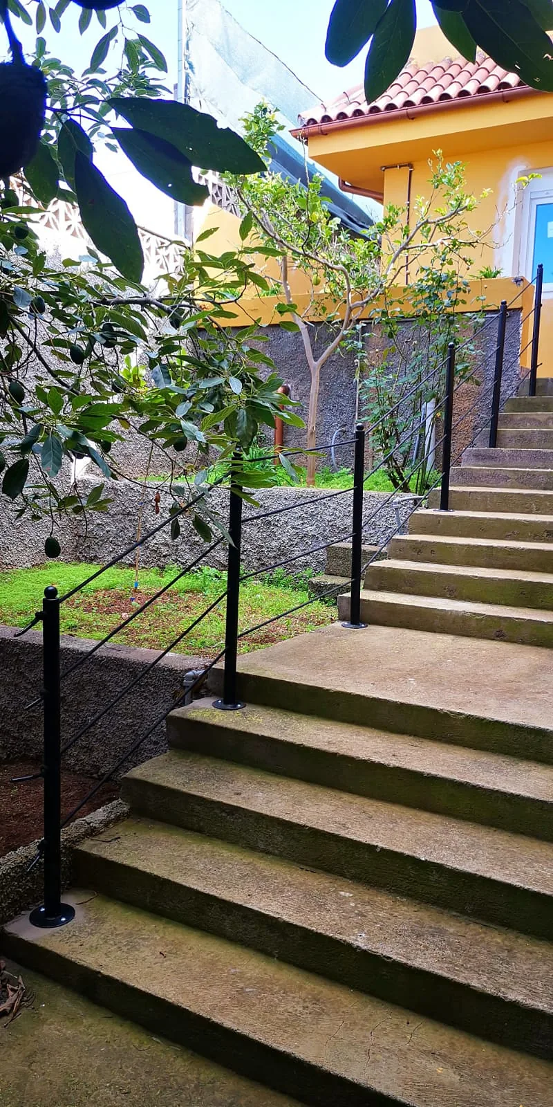Barandilla negra de postes redondeados y barras inclinadas en una escalera de jardín hacia una casa amarilla