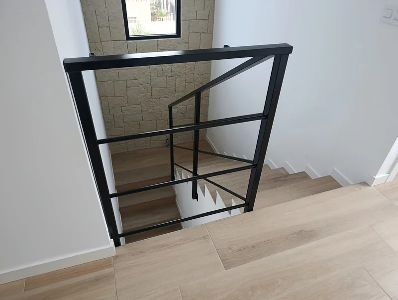 Barandilla negra de líneas horizontales alrededor de una escalera interior con peldaños claros
