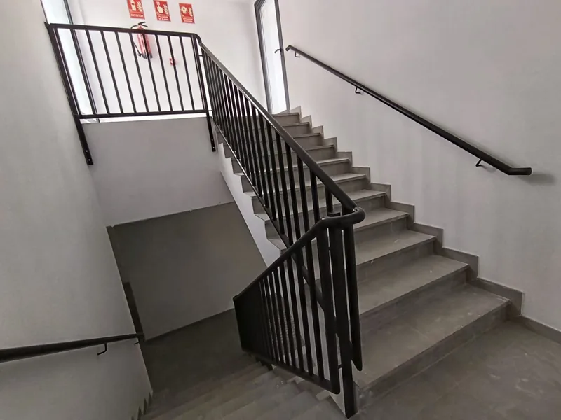 Barandilla negra de barrotes verticales y pasamanos de pared en una escalera interior con descansillo