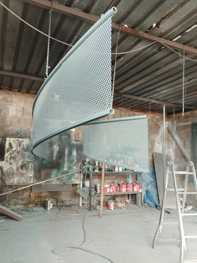 Panel curvo de chapa perforada con borde tubular suspendido durante el trabajo en taller