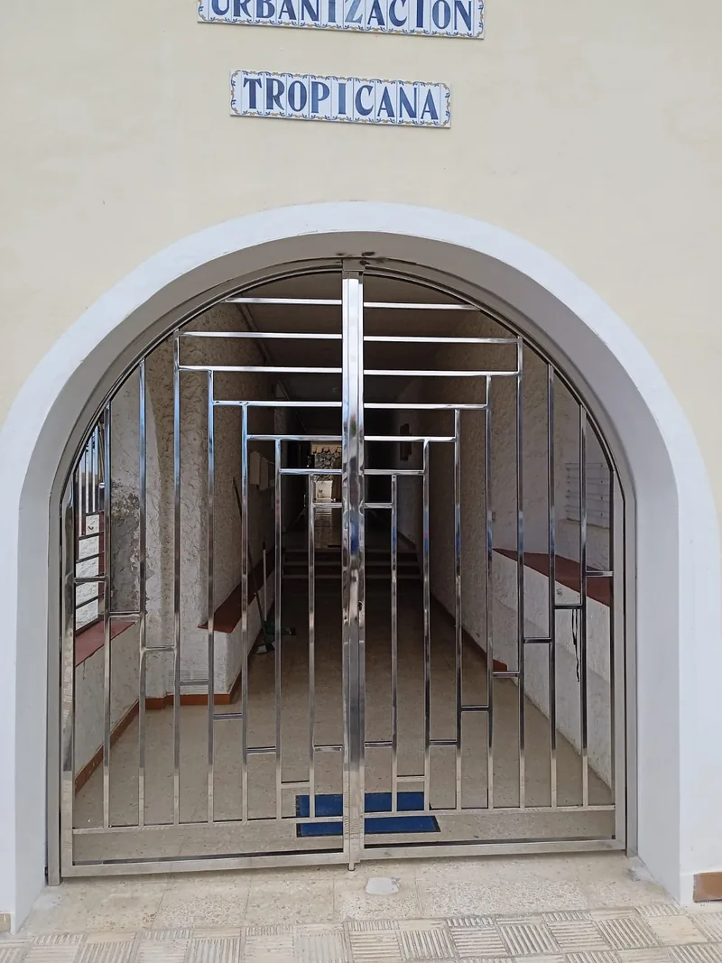 Cancela brillante de dos hojas con perfiles geométricos y marco superior adaptado a un arco