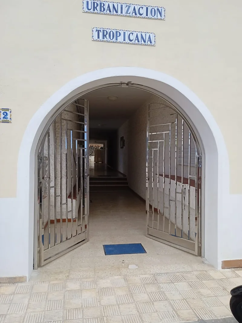 Dos hojas de una cancela metálica abiertas hacia el interior de un portal con arco