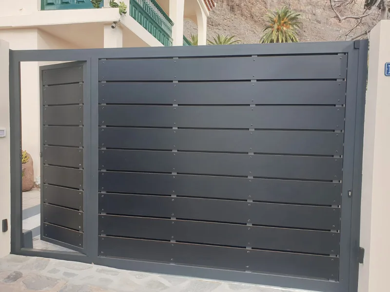 Cancela gris de lamas horizontales con puerta peatonal integrada abierta hacia el interior