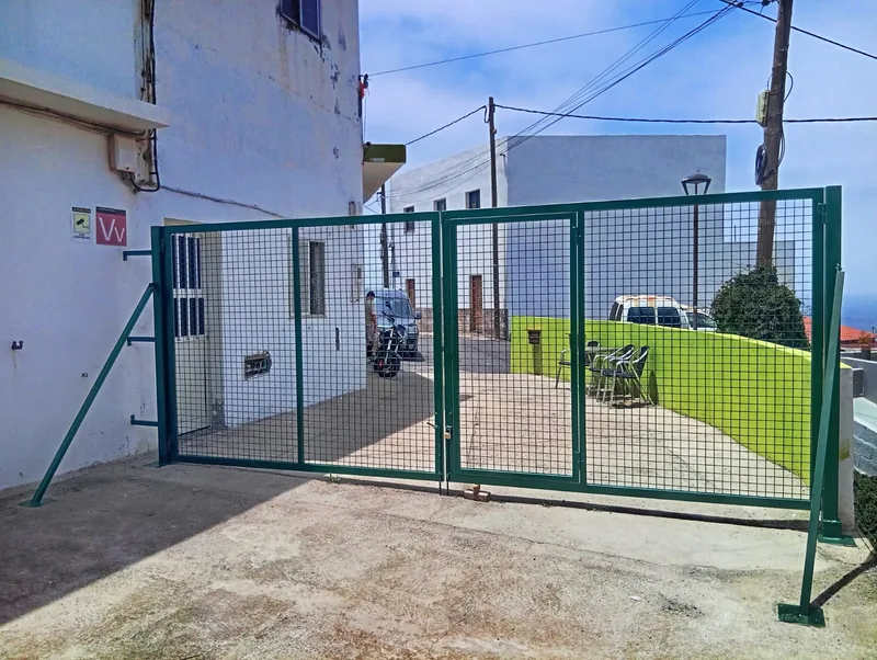 Cancela verde de dos hojas con malla de cuadrícula instalada junto a un edificio