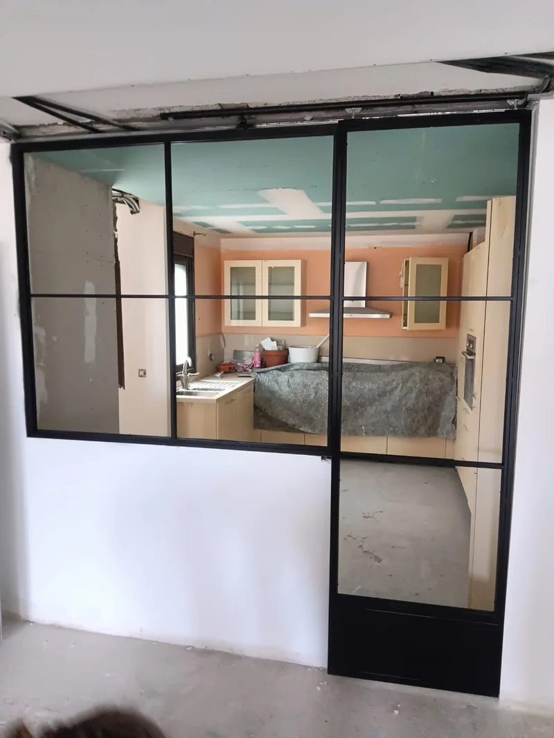 Cerramiento negro con paños transparentes y puerta lateral delante de una cocina en reforma