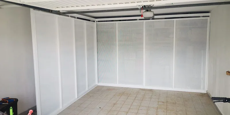 Cerramiento de marcos y paneles blancos en el fondo y un lateral de un garaje bajo las guías de su puerta