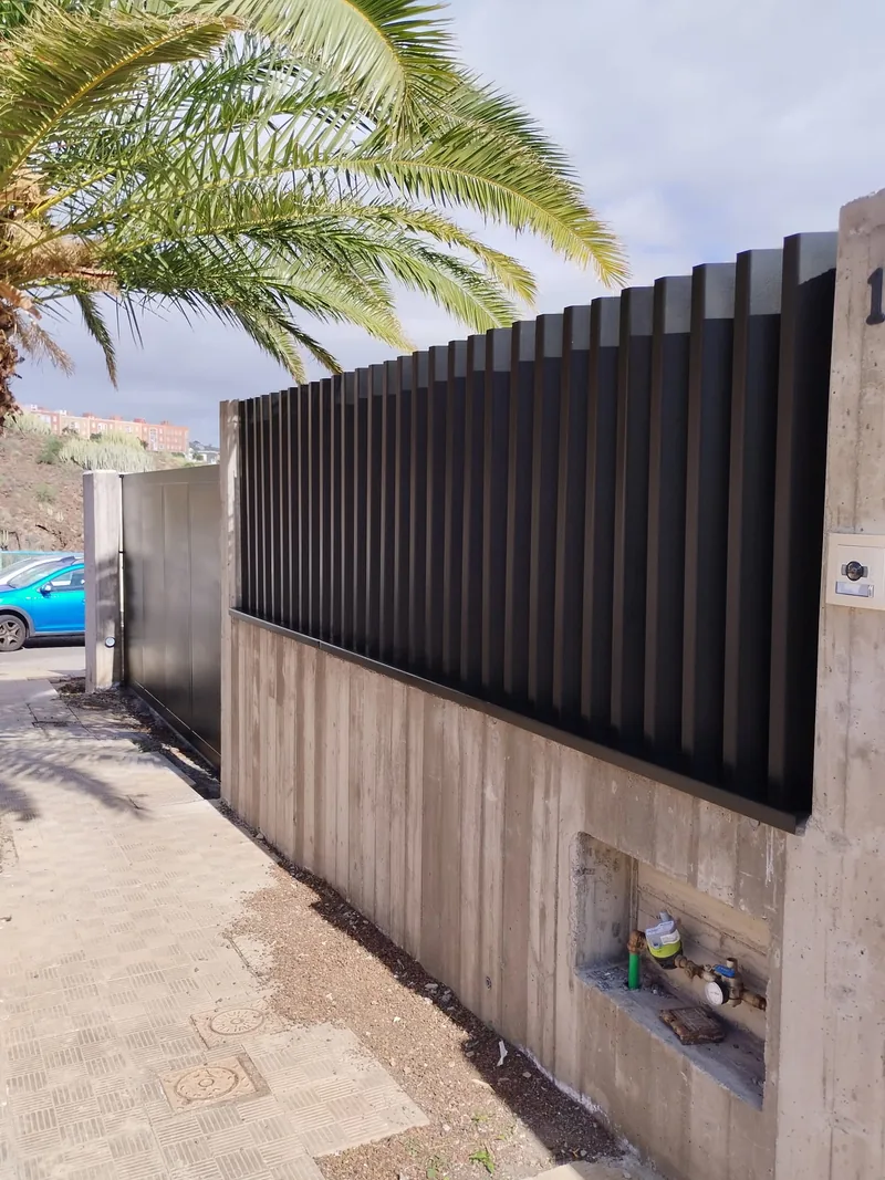 Cerramiento oscuro de lamas verticales sobre un muro de entrada junto a una puerta opaca