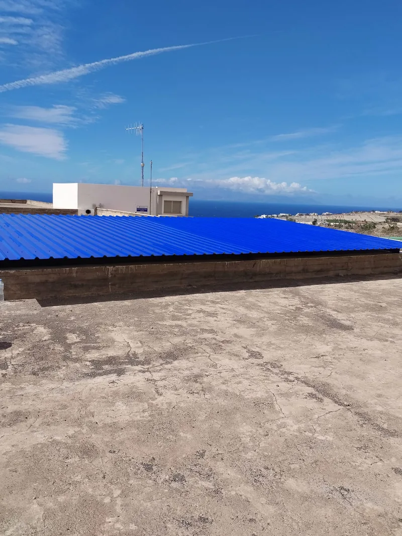 Cubierta rectangular de paneles acanalados azules sobre un hueco delimitado por muros bajos en una azotea