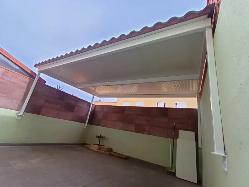 Cara inferior blanca de una cubierta de patio sostenida por perfiles metálicos junto a muros verdes