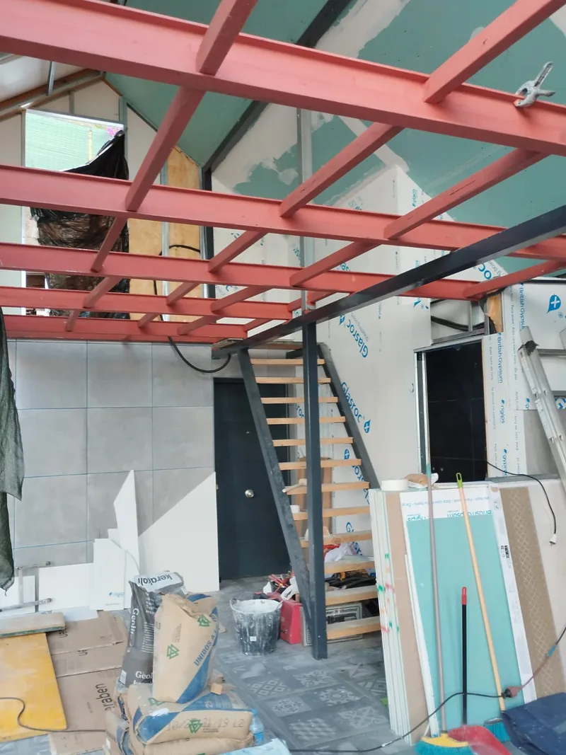 Vigas y travesaños rojizos sobre una escalera interior durante trabajos de reforma