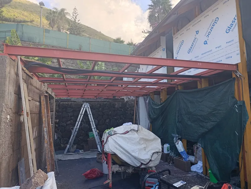 Frente de una estructura metálica rojiza adosada a una construcción durante una fase de cerramiento