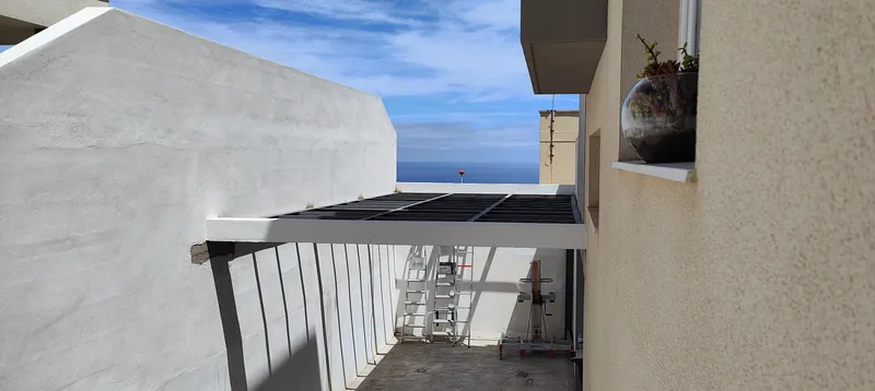Entramado metálico oscuro entre el muro blanco de un patio y la fachada de una vivienda