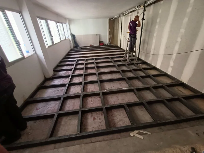 Retícula de perfiles metálicos sobre el suelo de una habitación alargada con ventanas laterales