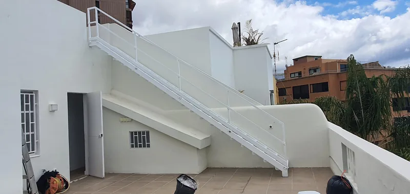 Escalera exterior blanca de tramo recto con barandilla junto a la fachada de una vivienda