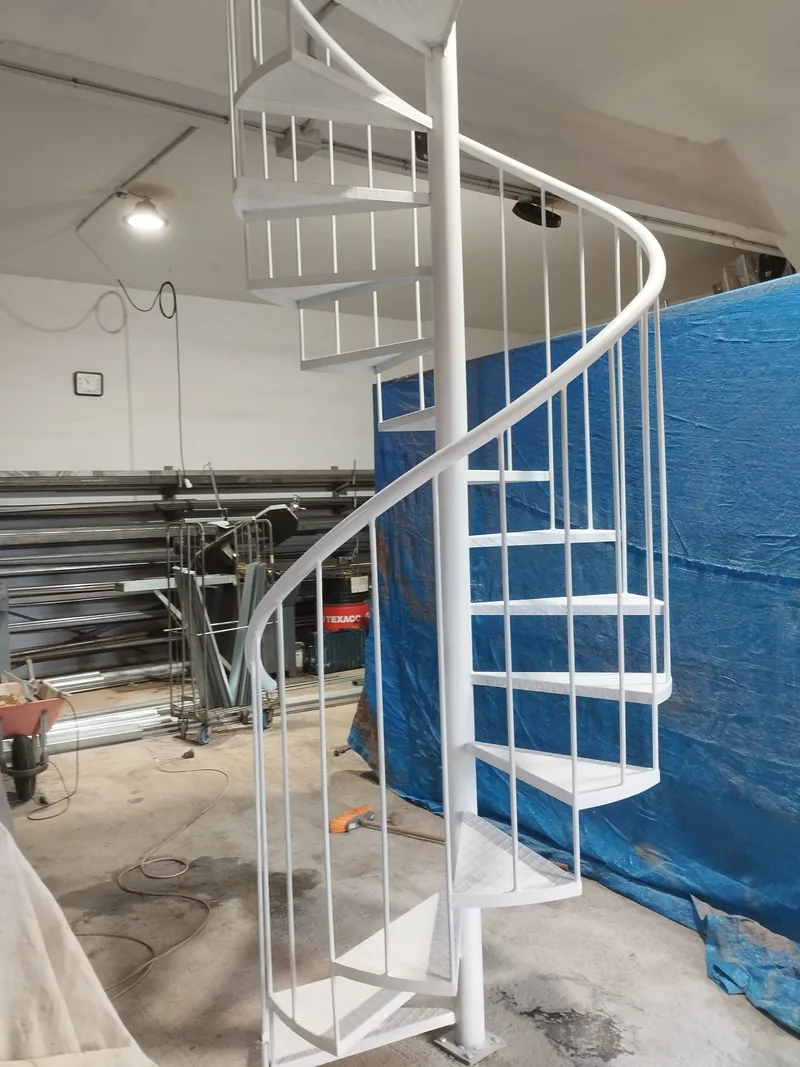 Escalera metálica de caracol blanca con eje central, peldaños triangulares y pasamanos curvo