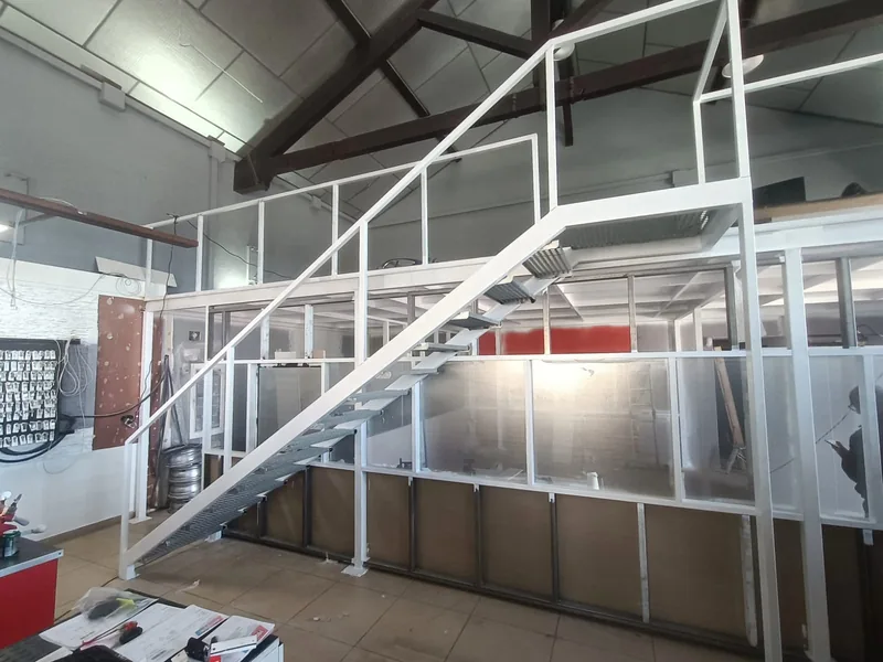 Escalera metálica blanca de tramo recto con peldaños de rejilla que sube a una entreplanta de un local