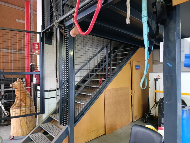 Escalera metálica oscura con paneles laterales de malla que sube a una plataforma interior