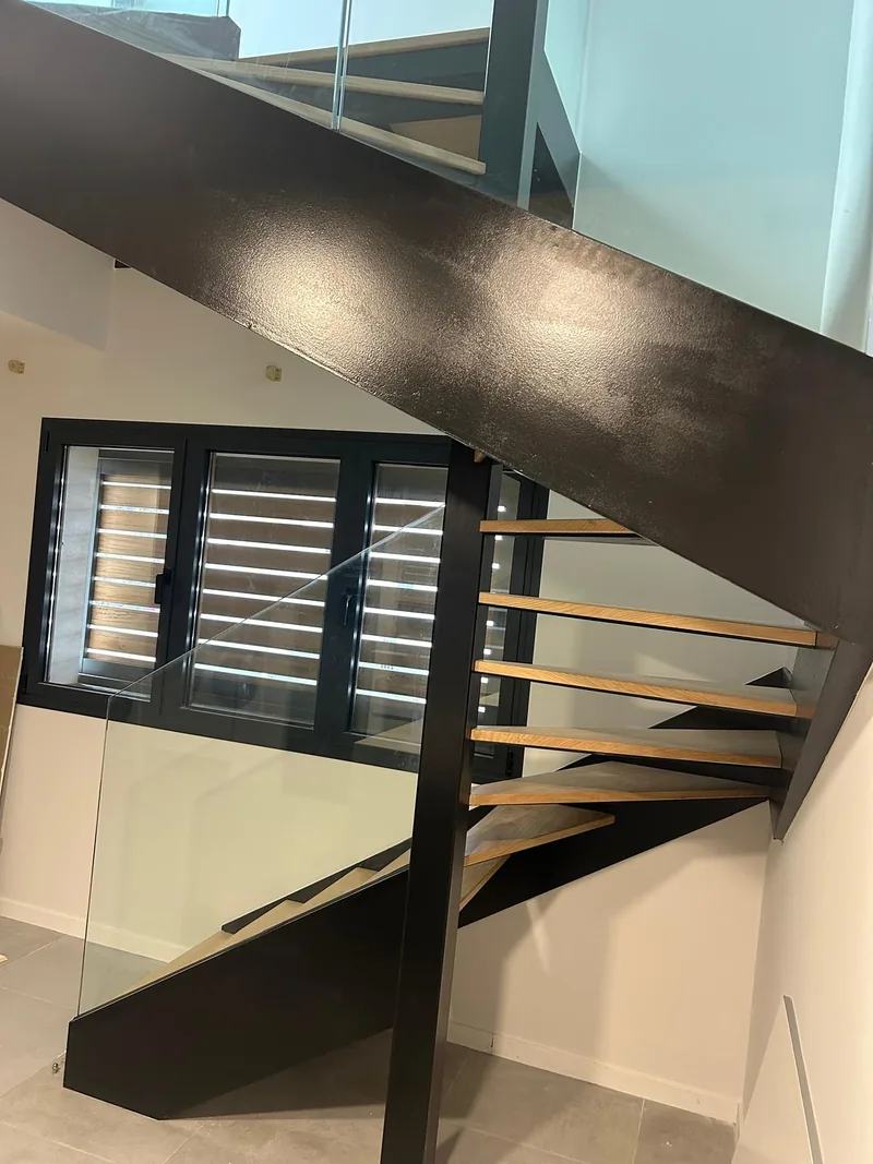 Escalera interior de estructura metálica oscura con peldaños de acabado madera y paneles transparentes