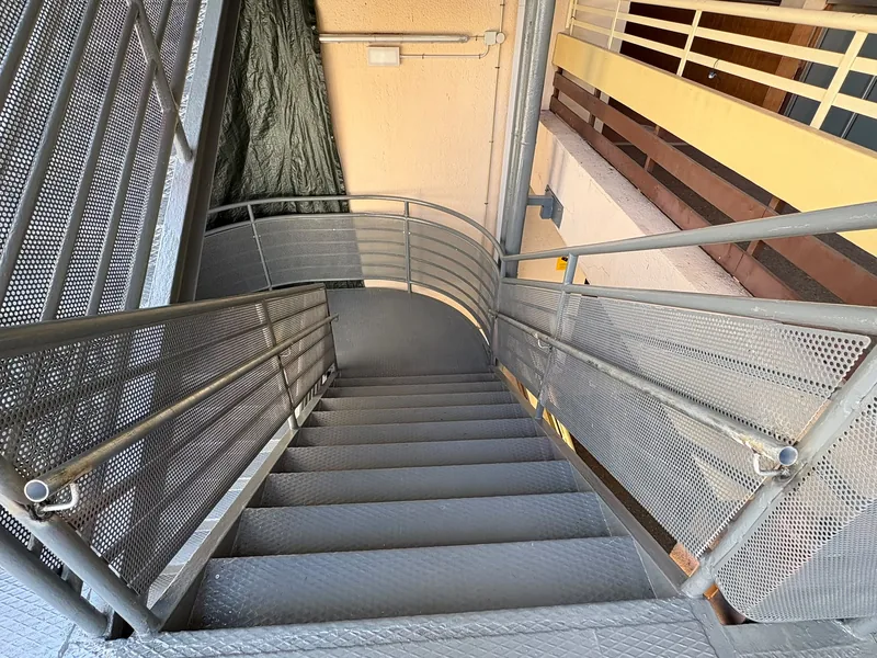 Escalera metálica gris vista desde arriba con descansillo curvo y barandillas de chapa perforada