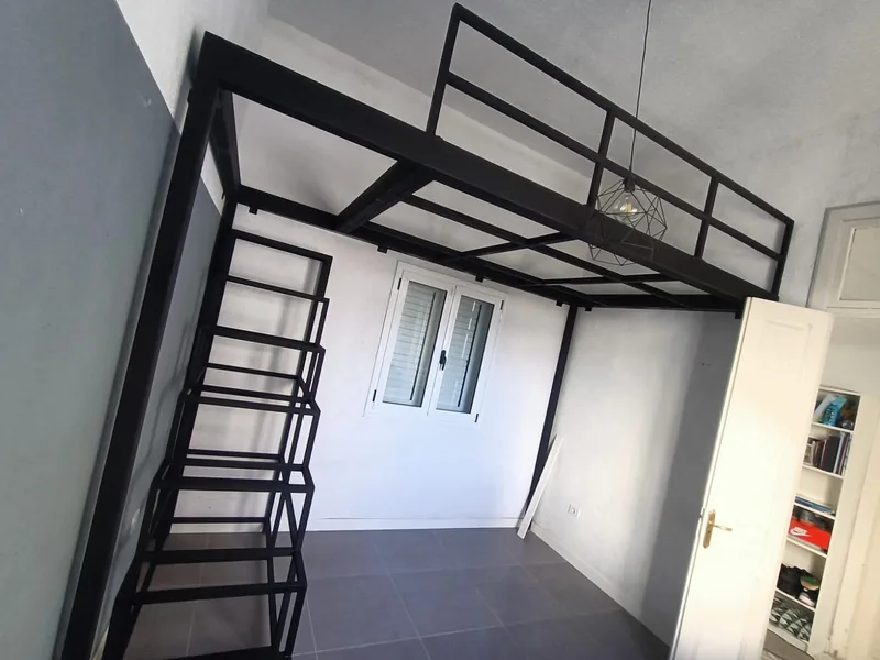 Estructura metálica negra para altillo con escalera lateral y barandilla en una habitación