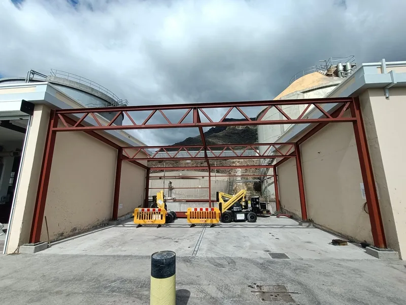 Vista frontal de una estructura de pilares y cerchas rojas durante una fase de montaje
