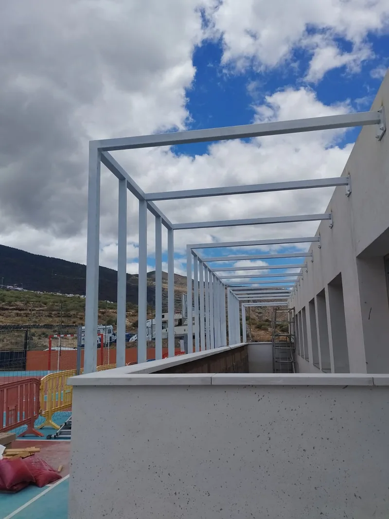 Sucesión de marcos metálicos blancos sobre un paso junto a un edificio y un patio