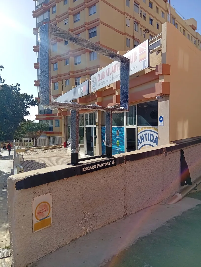 Marco rectangular oscuro sobre dos soportes fijados a un muro exterior junto a locales