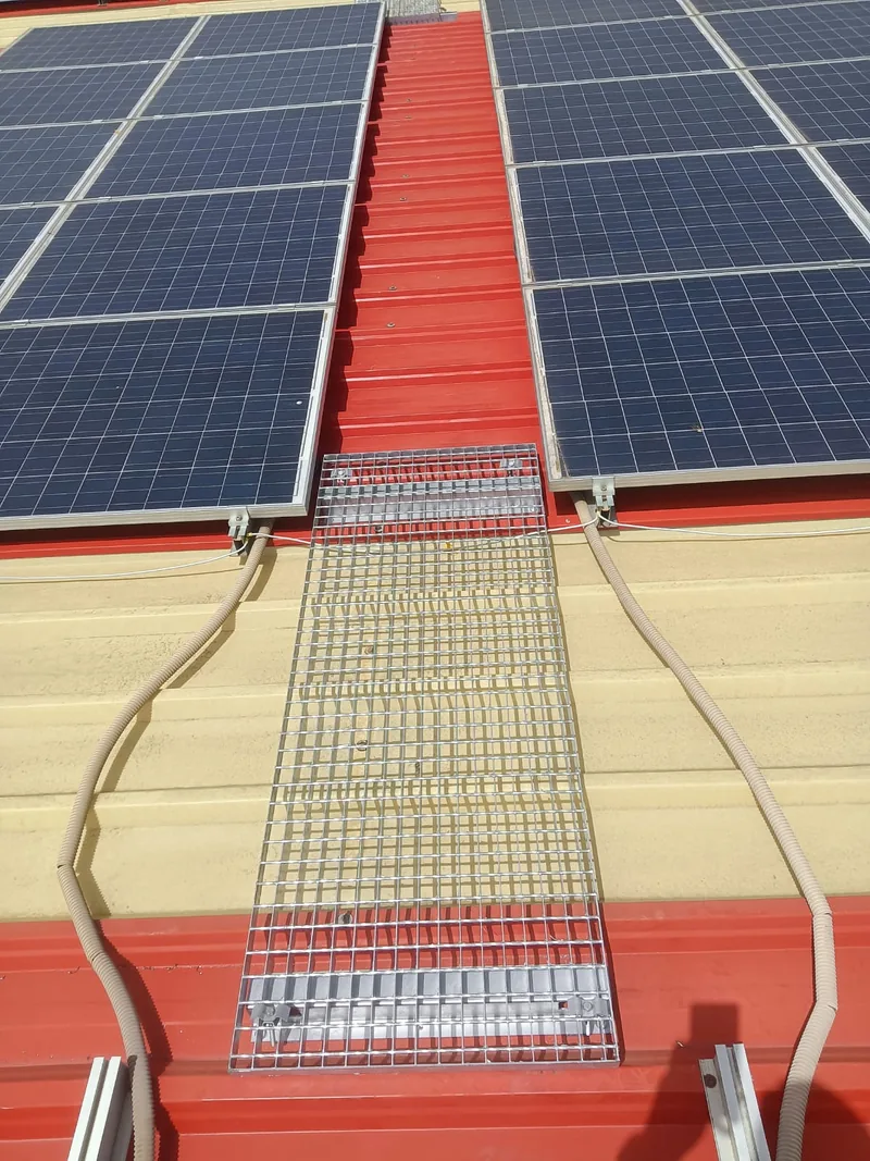 Módulo rectangular de rejilla metálica sobre una cubierta roja en la franja entre paneles solares