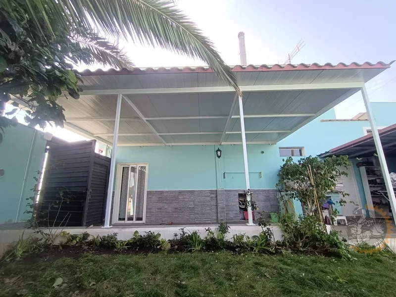 Pérgola blanca con cubierta gris frente a una vivienda con jardín
