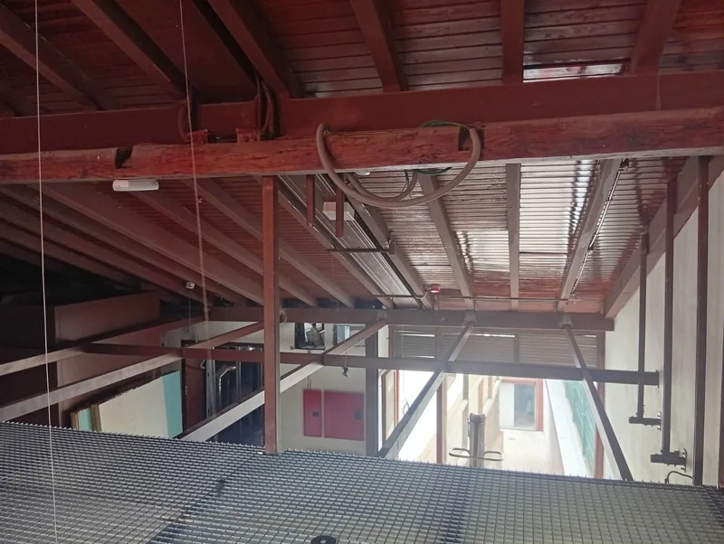 Entramado de perfiles rojizos junto a una plataforma de rejilla bajo un techo inclinado