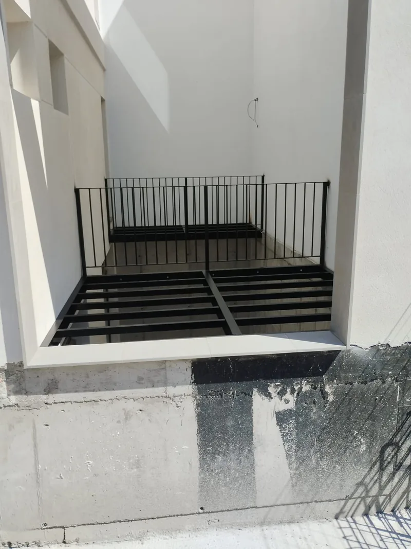 Dos entramados metálicos negros con barandillas verticales entre paredes blancas de un patio