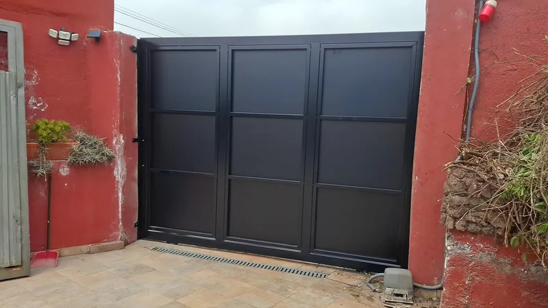Portón negro de paneles rectangulares entre dos muros rojizos