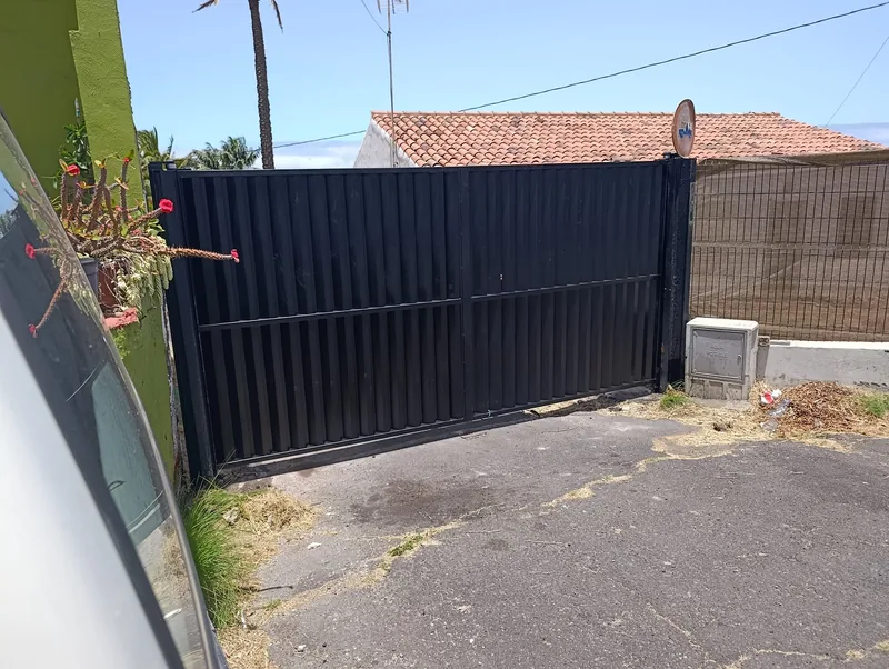 Portón oscuro de chapa con dibujo vertical y perfil horizontal visto desde el interior de una parcela