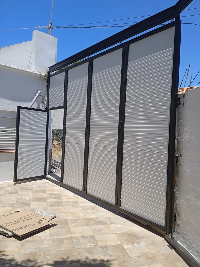 Interior del portón de paneles claros con la hoja peatonal abierta hacia el patio