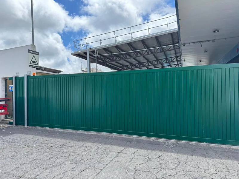 Portón industrial verde de paneles verticales instalado frente a una entrada cubierta