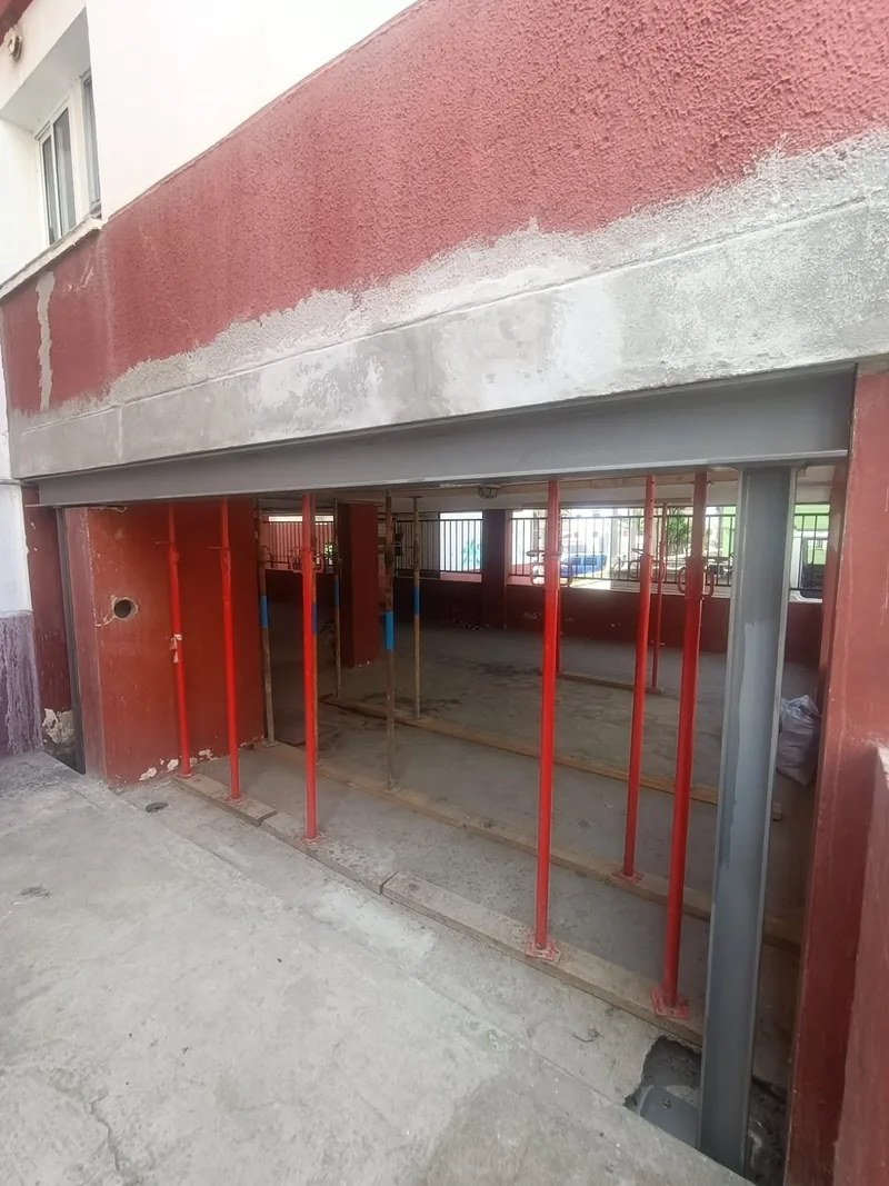 Viga y pilares metálicos grises en un hueco de fachada con puntales rojos en el interior